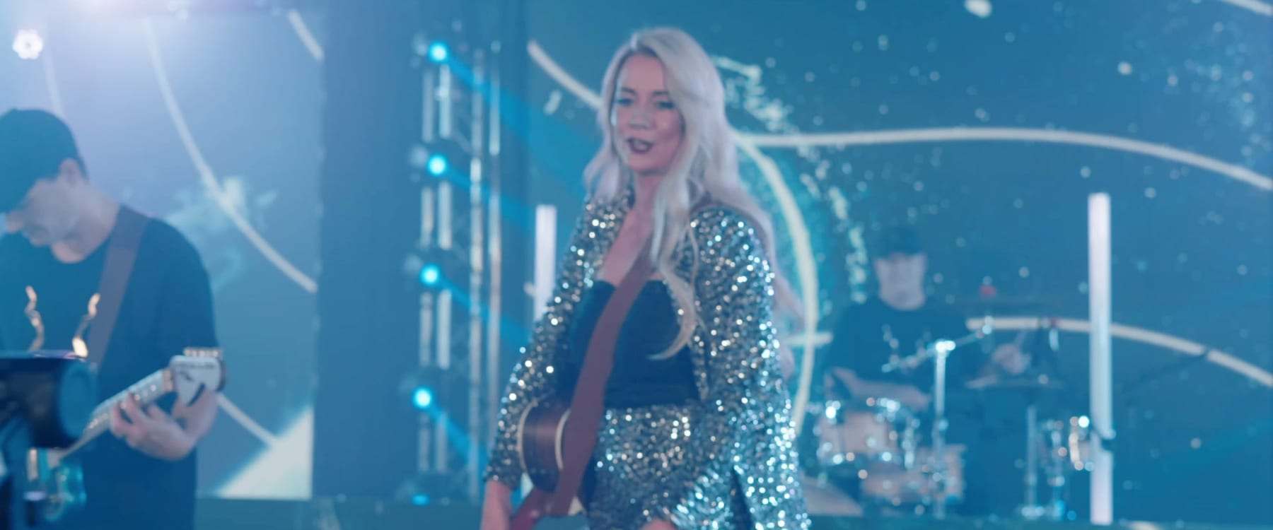 Cordelia smiling on stage with her guitarist and drummer under blue light