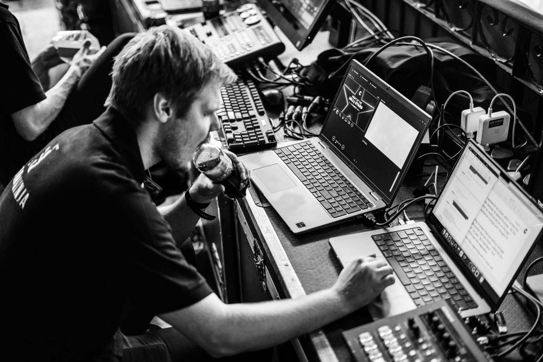 A crew member running the show from laptops at the desk, in black and white