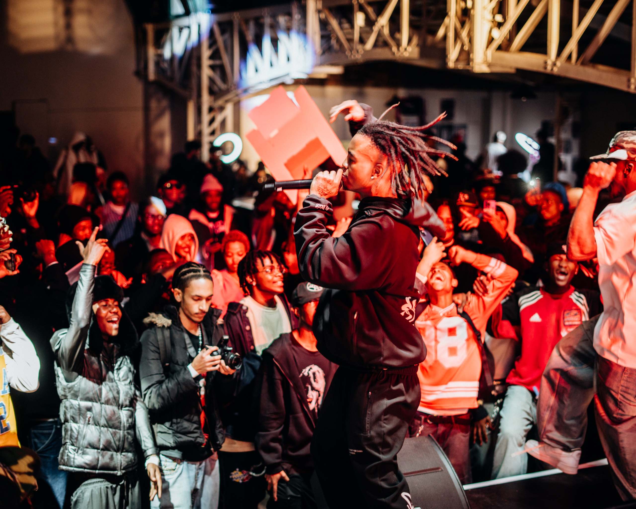 A packed crowd at a hip-hop show under truss and moving lights