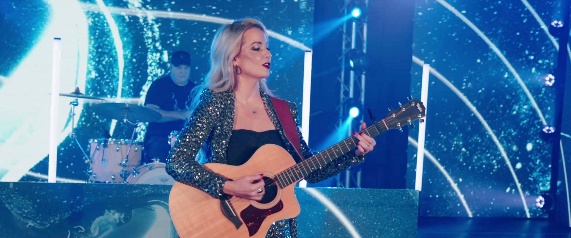 Cordelia playing guitar on stage in front of an LED screen, with her drummer behind her