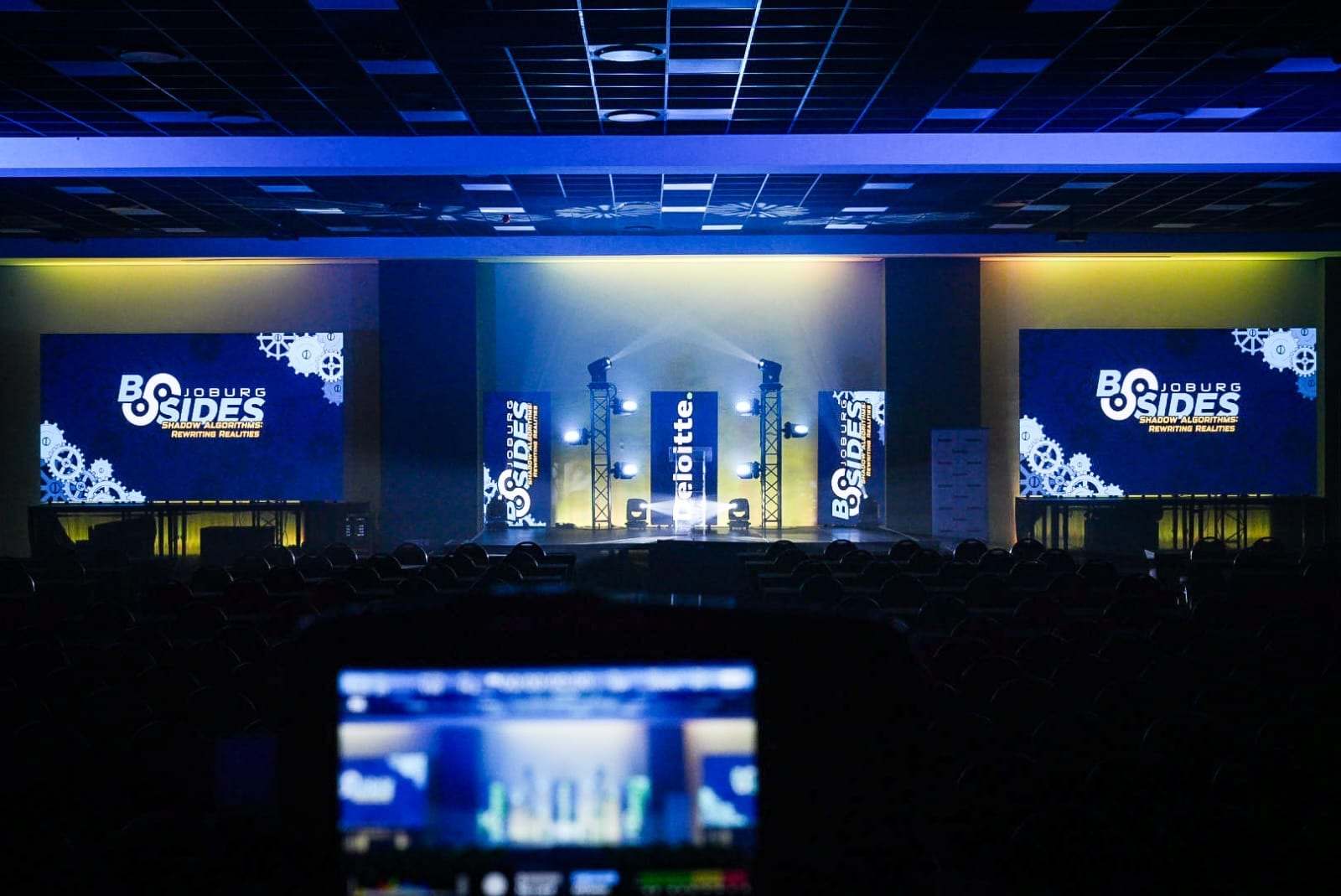 The BSides stage from the back of the room, with the LED screens and beams