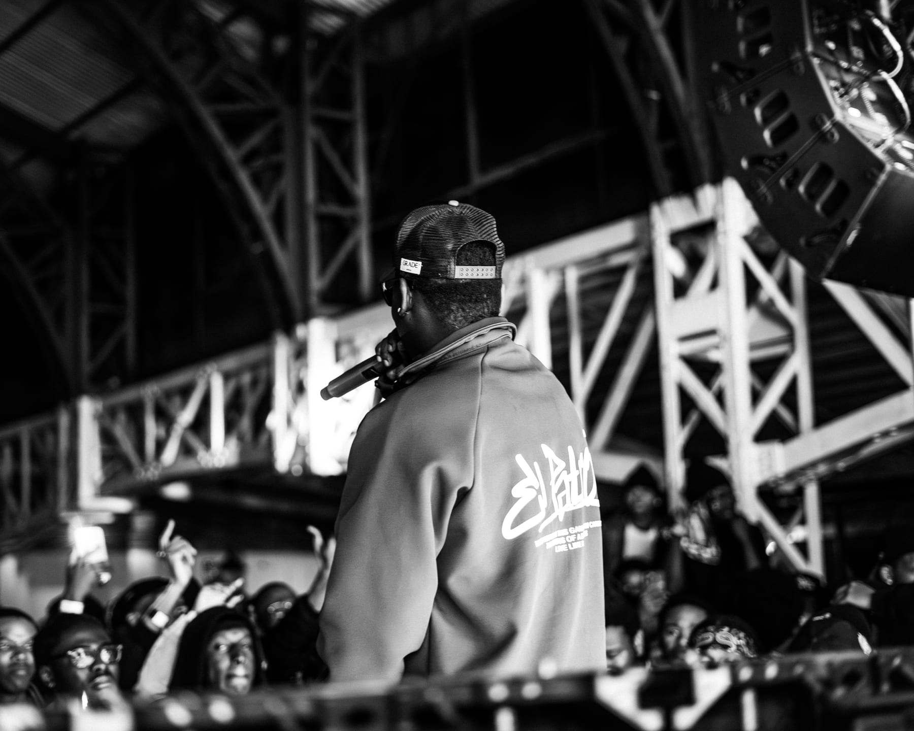 A rapper facing the crowd with the flown line-array PA above, in black and white