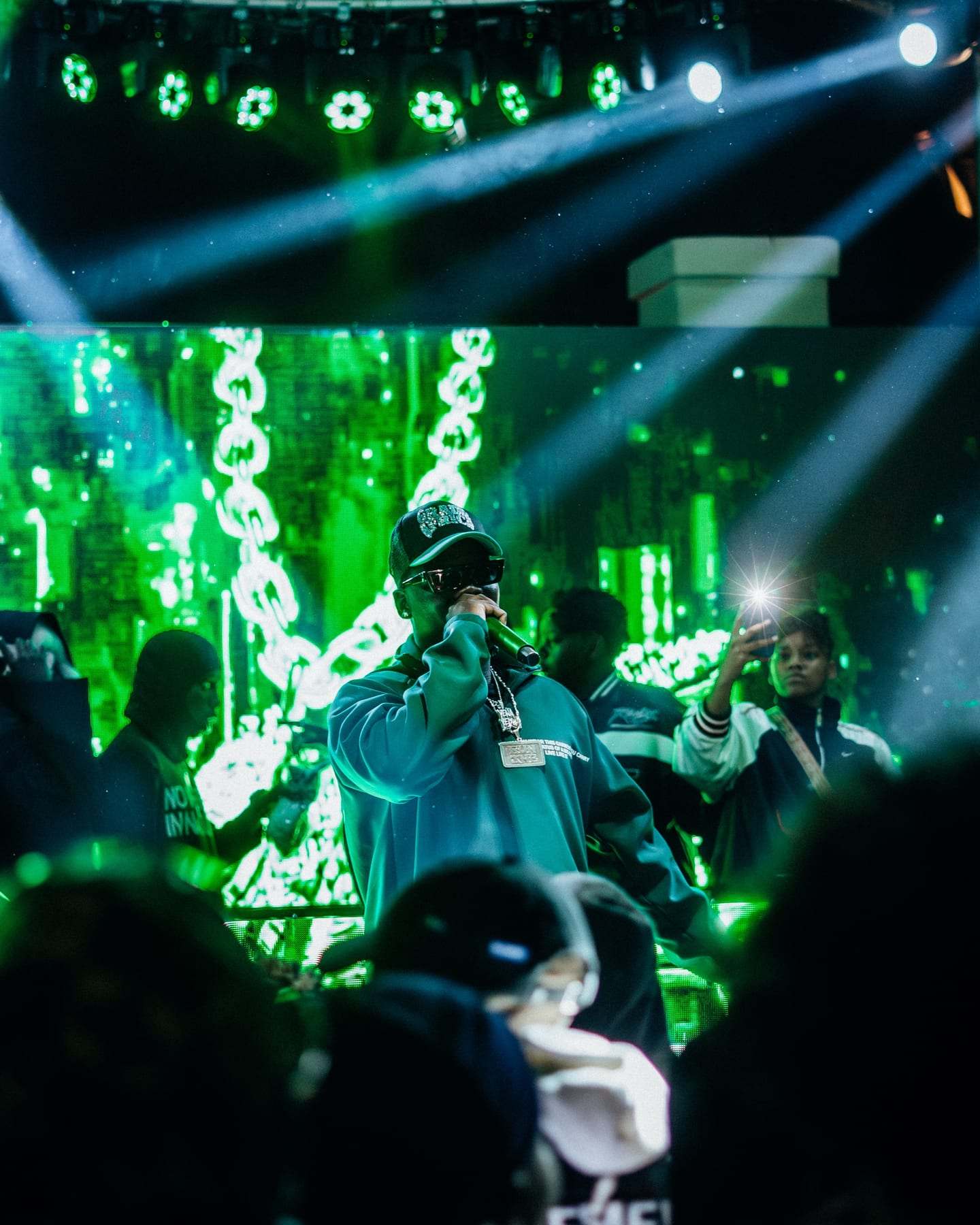 A rapper performing under green beams and haze