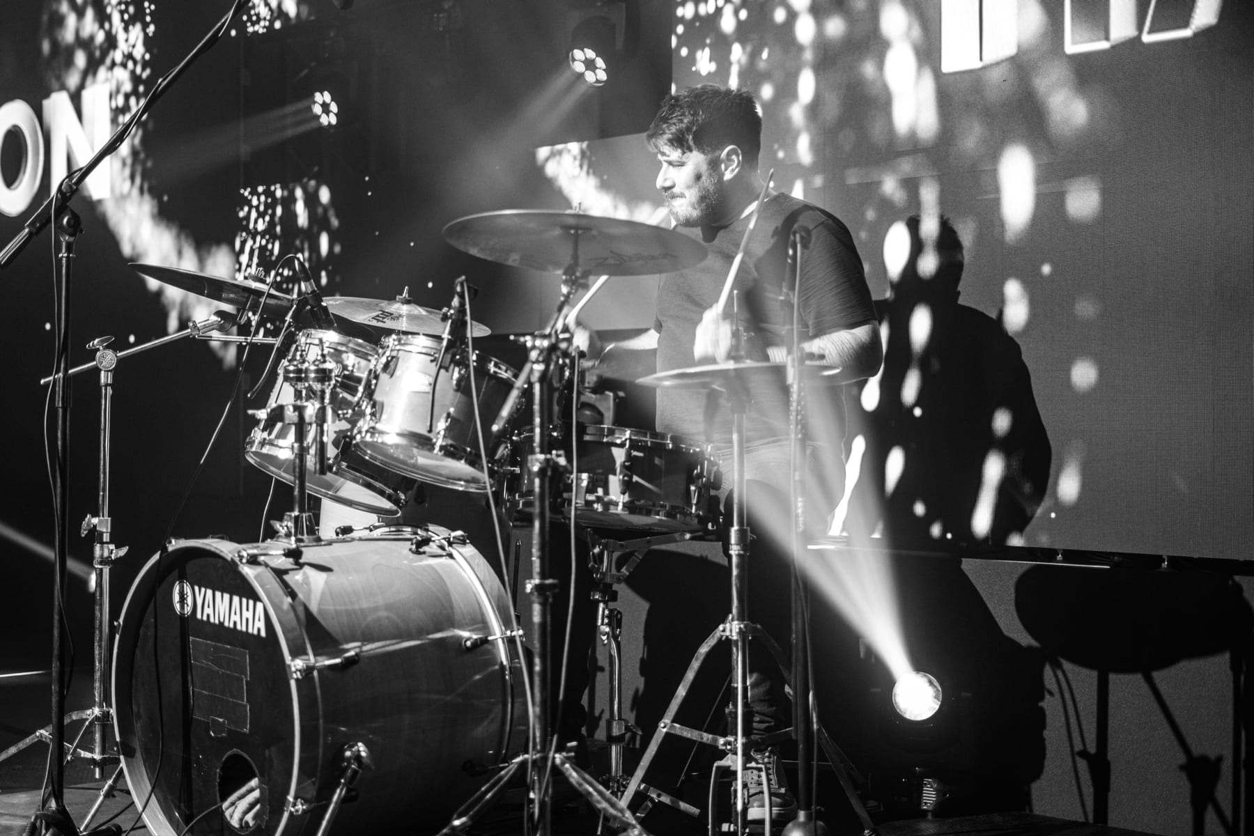 The live band's drummer under a beam, in black and white