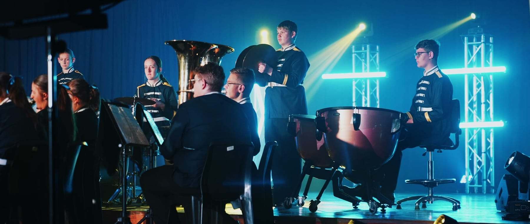 The school band with brass and timpani on stage under blue light