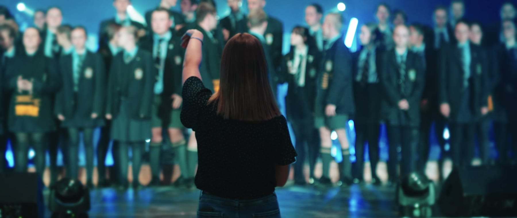 The school choir on stage with their conductor in front