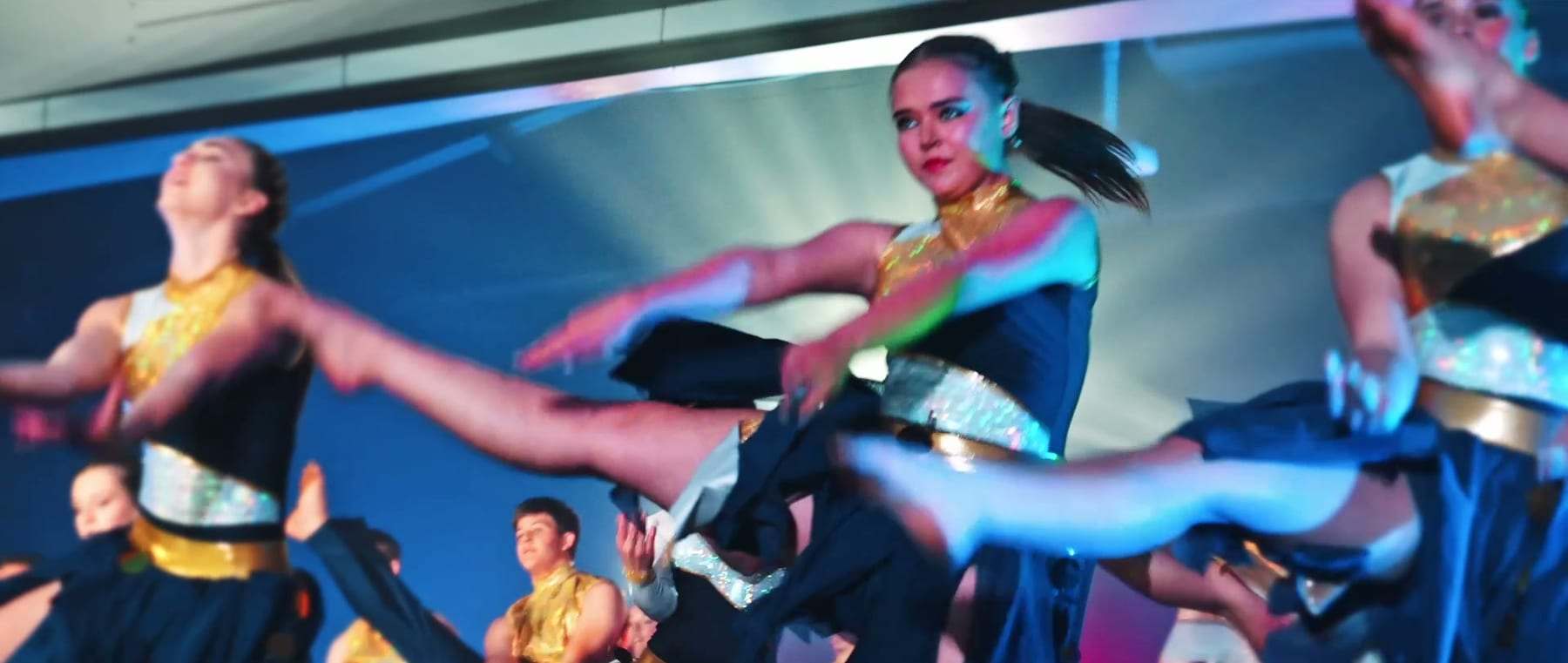 Dancers leaping mid-routine in gold and navy costumes
