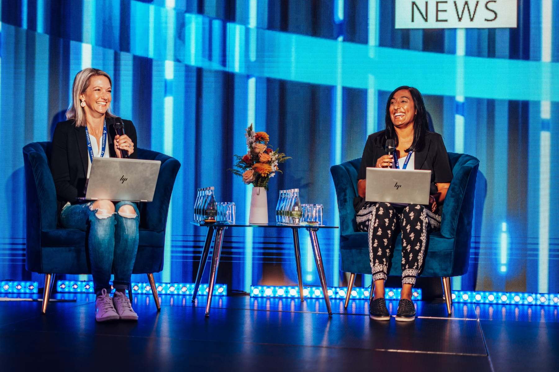 Two presenters on a news-desk style stage with a blue LED backdrop