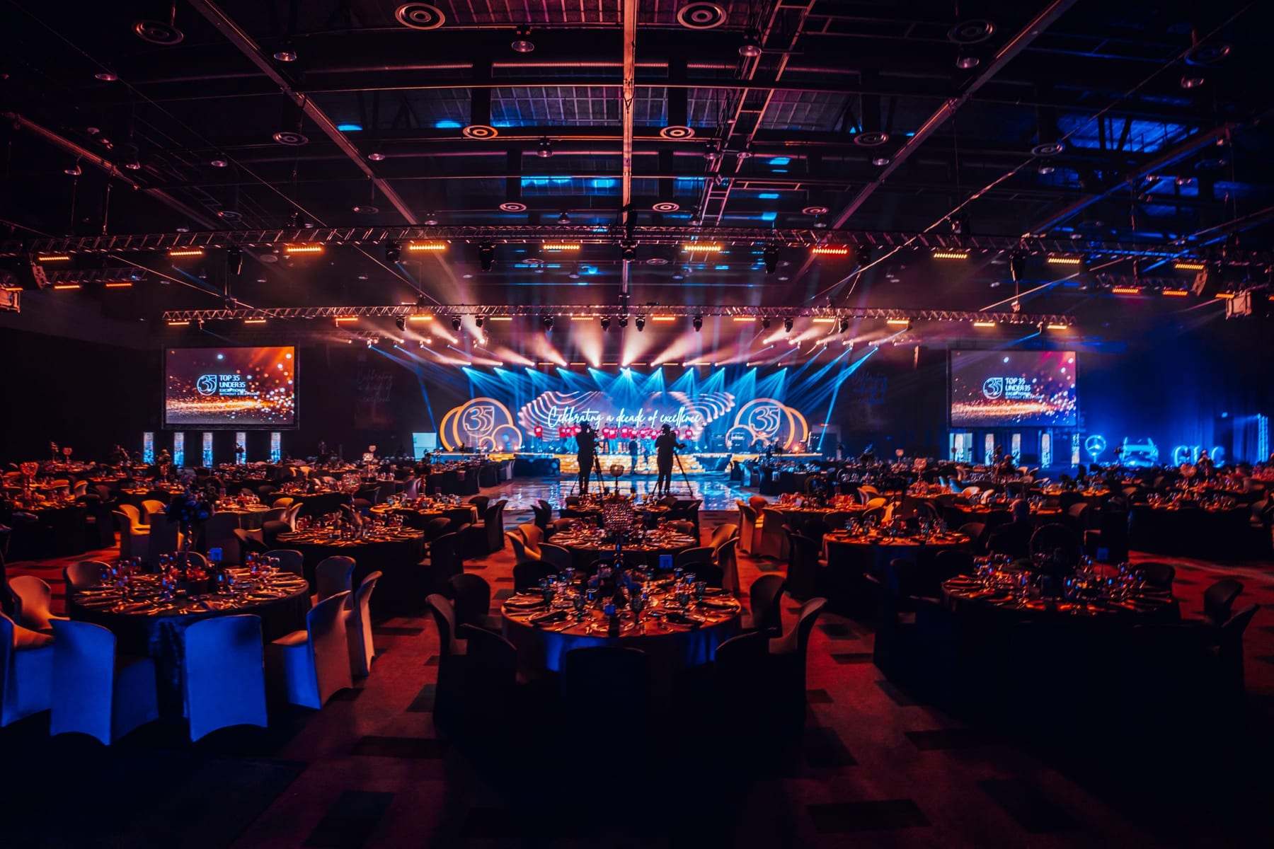 The full SAICA gala room from the back, with the stage, LED screens and beams over the tables