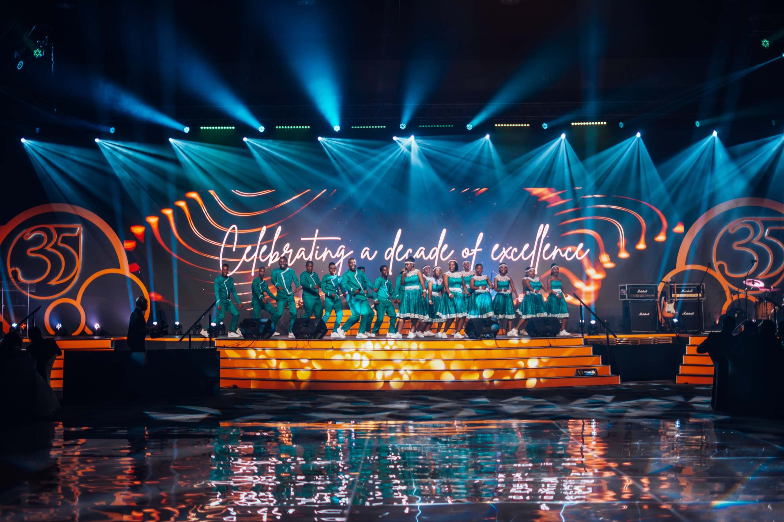 A choir on stage at the SAICA gala, lit with beams in front of the LED wall