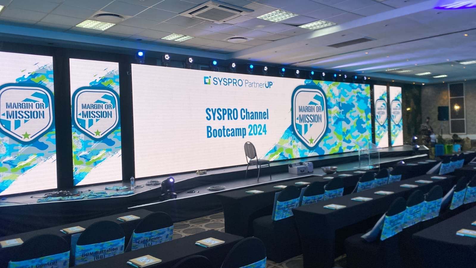 A wide LED wall reading SYSPRO Channel Bootcamp 2024 across the front of the room