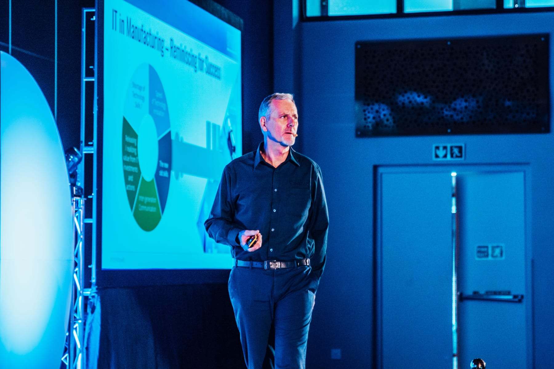 A speaker presenting in front of a slide on the big screen