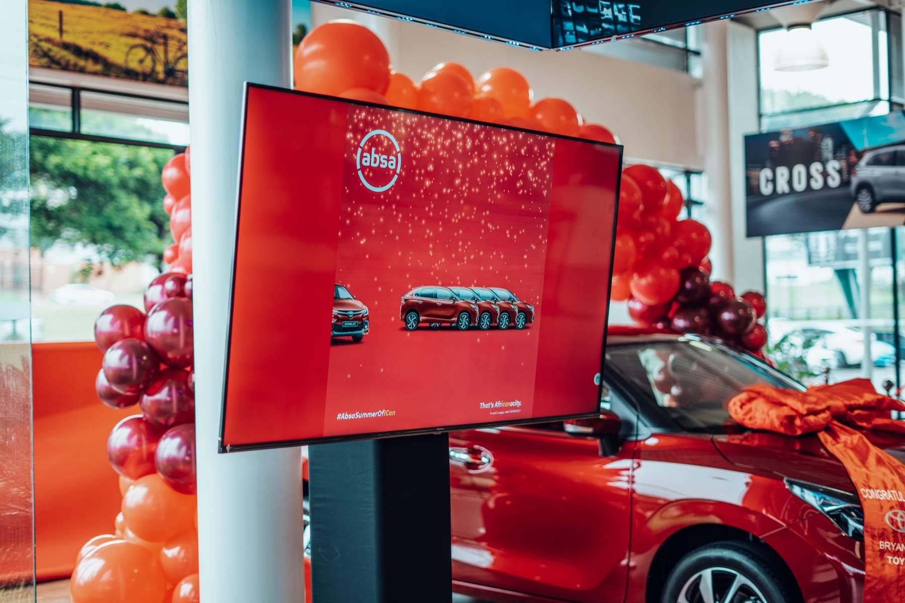 A screen on a stand with Toyota graphics next to the car